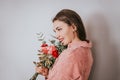 A woman in a pink sweater holding a bouquet of flowers in front of a white background. Womad day 8 march