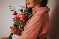 A woman in a pink sweater holding a bouquet of flowers in front of a white background. Womad day 8 march