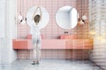 Woman in pink tile bathroom with double sink