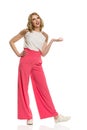 Woman In Pink Wide Legs Trousers Is Standing, Gesturing, Talking And Looking Away