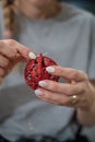 Woman with pink winter manicure tying a golden string on shiny red holiday bauble