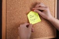 Woman pinning paper note with phrase Don`t Forget to cork board, closeup