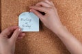 Woman pinning paper note with phrase Meeting On Friday to cork board, closeup