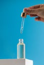 A woman with a pipette drips skin care serum into a transparent dropper, which stands on a podium