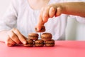 Woman placing macaroons on heap on pink table