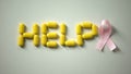 Woman placing pink ribbon near help word made of pills on table, breast cancer Royalty Free Stock Photo