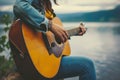 Woman playing acoustic guitar by lake, girl strumming guitar Royalty Free Stock Photo