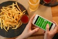 Woman playing game using smartphone at table with snacks, top view