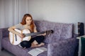 30 woman playing the guitar, sitting on the sofa in home interior. Lovely young girl learning to play the guitar with music sheets Royalty Free Stock Photo