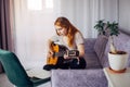 30 woman playing the guitar, sitting on the sofa in home interior. Lovely young girl learning to play the guitar with music sheets Royalty Free Stock Photo