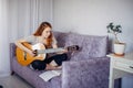 30 woman playing the guitar, sitting on the sofa in home interior. Lovely young girl learning to play the guitar with music sheets Royalty Free Stock Photo