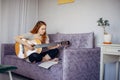 30 woman playing the guitar, sitting on the sofa in home interior. Lovely young girl learning to play the guitar with music sheets Royalty Free Stock Photo