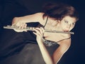 Woman playing transverse flute on black.