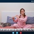 A woman plays a flute while sitting on a bed in an online video chat. Screen with chat and video call interface