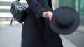 Woman plays with modern black hat moving wide-brimmed chapeau at black coat bottom in street slow motion low angle shot.