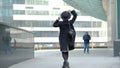 Woman plays with modern black hat moving wide-brimmed chapeau at black coat bottom in street slow motion low angle shot.