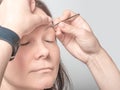 Woman plucking eyebrows with tweezers at home close up