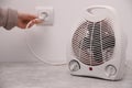 Woman plug in modern electric fan heater indoors, focus on device. Space for text Royalty Free Stock Photo