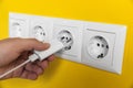 Woman plugging charger into power socket on yellow wall, closeup. Electrical supply