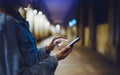 Woman pointing finger on blank screen smartphone on background bokeh light in night atmospheric city, hipster using in hands clean