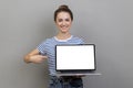 Woman pointing finger at laptop with white blank display, bragging with internet advertisement. Royalty Free Stock Photo