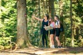 Woman points her hand at a hiking trail sign on a tree, while teenage girls study a hiking map