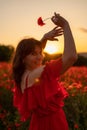 Woman poppy field red dress sunset. Happy woman in a long red dress in a beautiful large poppy field. Blond stands with Royalty Free Stock Photo