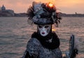 Woman poses in ornate, detailed costume, mask and hat outside San Giorgio Maggiore during Venice Carnival, Italy.