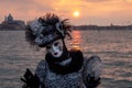 Woman poses in ornate, detailed costume, mask and hat outside San Giorgio Maggiore during Venice Carnival, Italy.