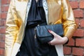 Woman poses for photographers with shiny golden jacket and black leather bag before Fendi fashion show, Milan