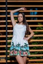 A woman is posing in a dress on a street and on a wooden background. The charming lady with dark hair is enjoying a sunny day.