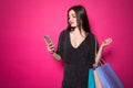 Image of a beautiful woman posing holding shopping bags using mobile phone  over pink background Royalty Free Stock Photo