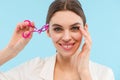 Woman posing over blue background holding lash curler doing makeup