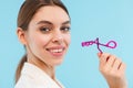 Woman posing over blue background holding lash curler doing makeup