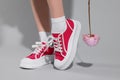 Woman posing in red classic old school sneakers with beautiful flower on light gray background, closeup Royalty Free Stock Photo