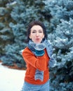 Woman is posing in winter forest, beautiful landscape with snowy fir trees. Dressed in red sweater. Blowing a kiss Royalty Free Stock Photo