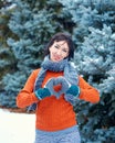 Woman is posing in winter forest, beautiful landscape with snowy fir trees. Dressed in red sweater. Showing a heart gesture Royalty Free Stock Photo