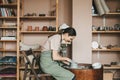 Woman pottery maker works in clay studio on pottery wheel against shelves with vases and pots. Royalty Free Stock Photo