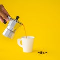 Woman poured Moka coffee into the white cup with roasted, coffee beans on a yellow paper background. Copy space for your text Royalty Free Stock Photo