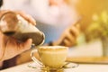 A woman poured the syrup into the saucer of the coffee cup while absent-mindedly playing the smartphone. Selective focus on the