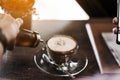 A woman poured the syrup into the saucer of the coffee cup while absent-mindedly playing the smartphone. Selective focus on the