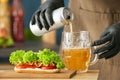 Woman pouring beer from tin can into glass mug on table with tasty hot dog Royalty Free Stock Photo