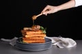 Woman pouring chicken drumstick and waffles with honey against dark background