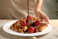 Woman pouring chocolate sauce onto tasty homemade waffles, closeup