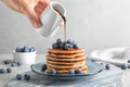 Woman pouring chocolate syrup onto fresh pancakes with blueberries at grey table