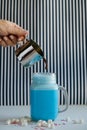 Woman is pouring coffee in cup of colored blue milk on a black-and-white background. Milk shake, cocktaill, frappuccino. Unicorn c