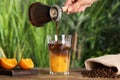 Woman pouring coffee into glass with orange juice and ice cubes at wooden table, closeup Royalty Free Stock Photo