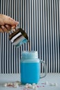 Woman is pouring coffee in stylized mason jar cup of colored blue milk on a black-and-white background. Milk shake, cocktaill, fra