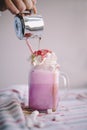 Woman is pouring coffee in stylized mason jar cup of colored milk with cream, marshmallow and colorful decoration. Milk shake, coc Royalty Free Stock Photo