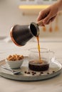 Woman pouring coffee from turkish pot into glass cup at white table, closeup Royalty Free Stock Photo